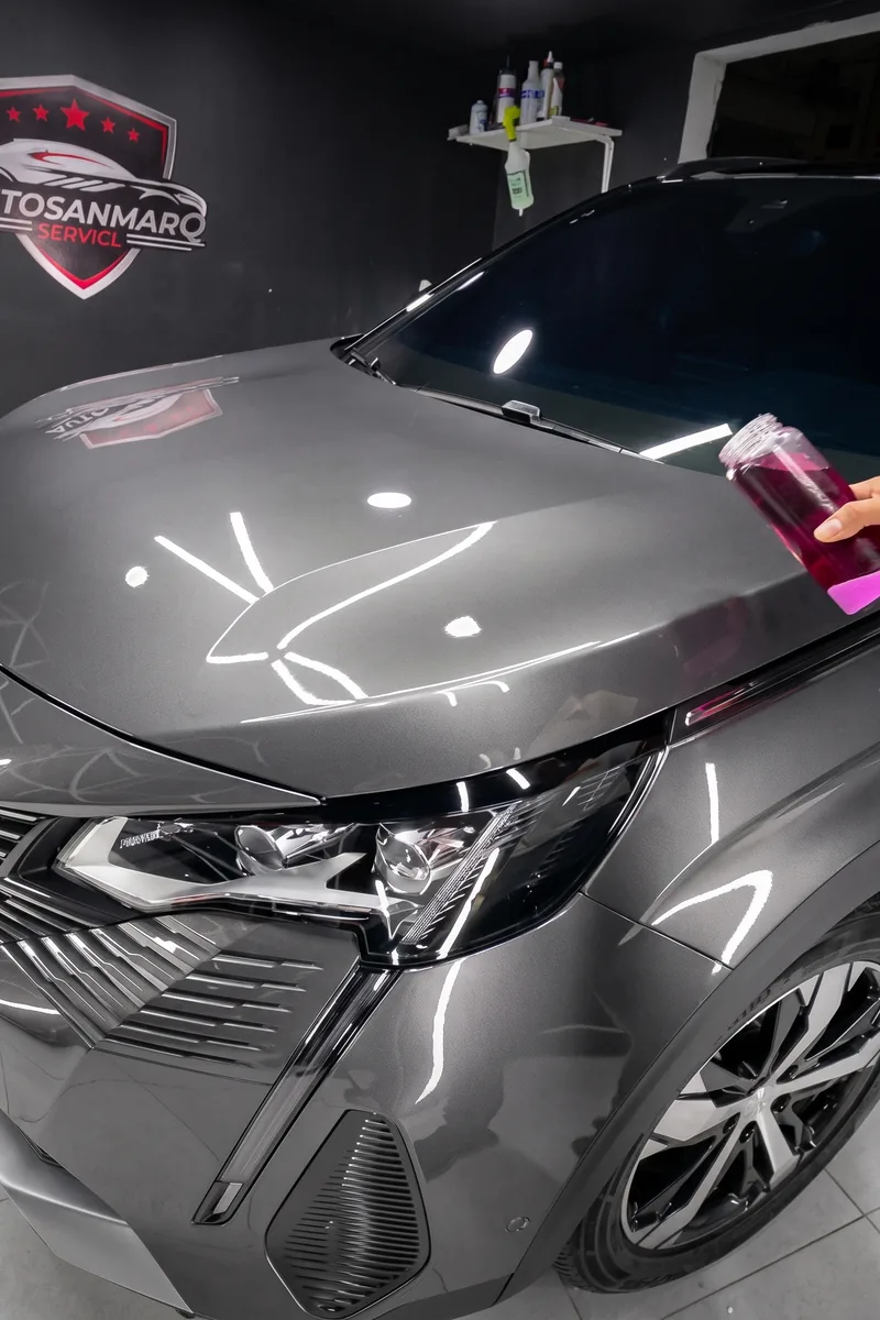 Capó de un carro gris recién pulido, con el reflejo de las luces del taller